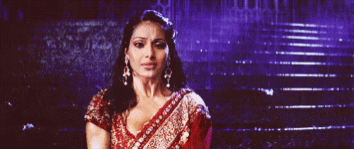 a woman in a red and gold saree is standing in front of a set of stairs .