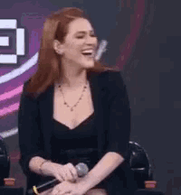 a woman is sitting in a chair with a microphone in her hand and laughing .