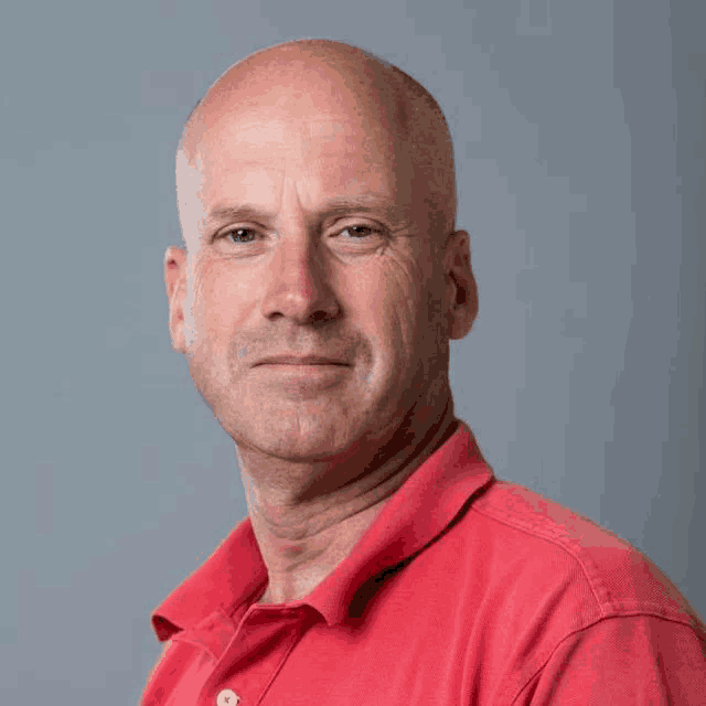 a bald man wearing a red polo shirt is looking at the camera