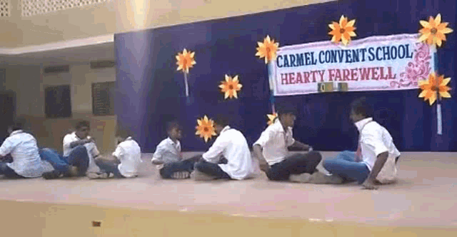 a group of young men sit on the floor in front of a banner that says carmel convent school
