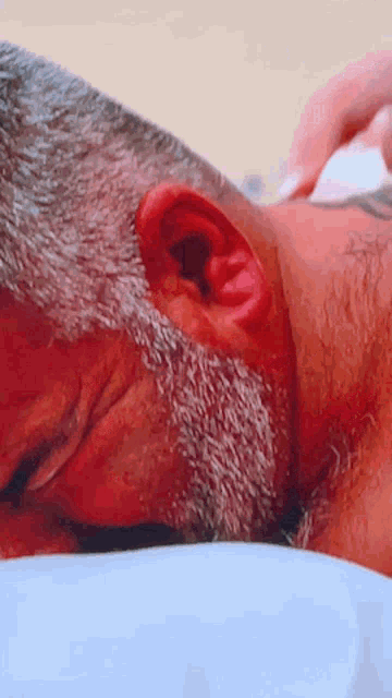 a close up of a man 's ear with a beard laying on a bed .