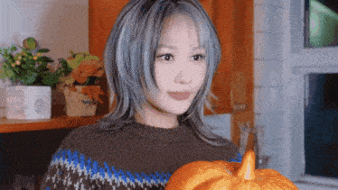 a woman in a brown and blue sweater holds a pumpkin