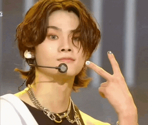 a young man with long hair is wearing a microphone and making a peace sign with his finger .