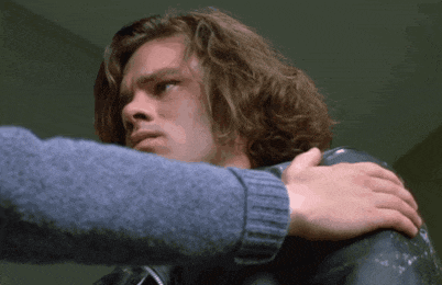 a man with long hair is being comforted by another man in a blue sweater