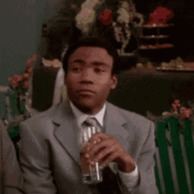 a man in a suit and tie is sitting on a bench holding a glass of beer .