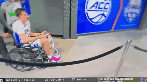 a man in a wheelchair is playing a video game in front of a banner that says acc