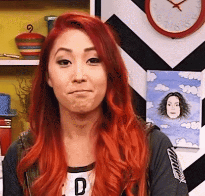 a woman with red hair is making a face in front of a clock and a painting .