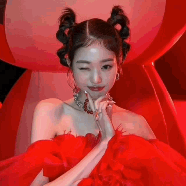 a woman in a red dress is winking at the camera while sitting in a red chair .