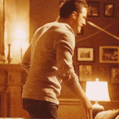 a man is standing in a living room with a lamp and pictures on the wall