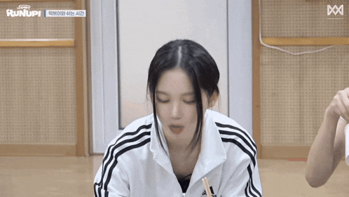 a woman wearing a white adidas jacket is sitting on the floor