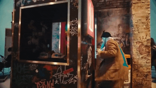 a man is standing in a room with graffiti on the wall and a trash can .