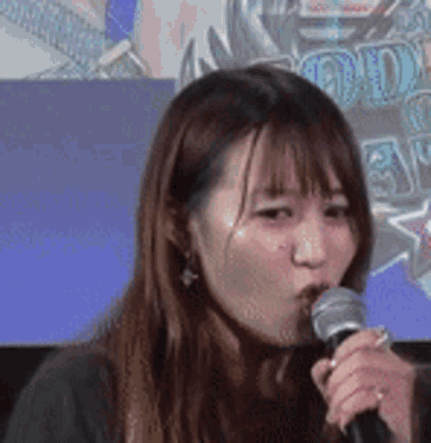 a woman is singing into a microphone while sitting in front of a sign .