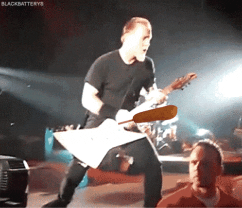 a man in a black shirt is playing a guitar on a stage with the words blackbatteries written above him