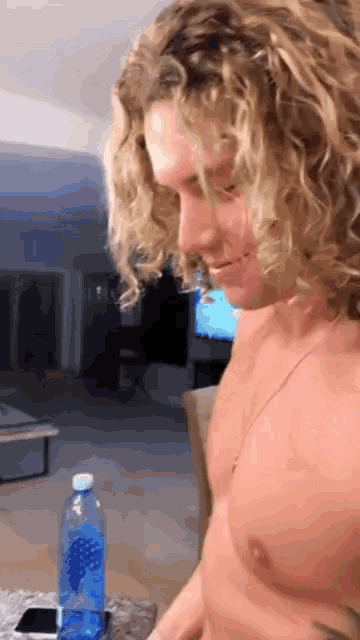 a shirtless man with curly hair looks down at a bottle of aquafina water