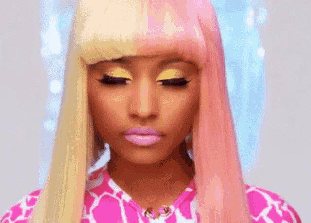 a woman with pink hair and yellow eyeshadow is wearing a pink and yellow shirt .