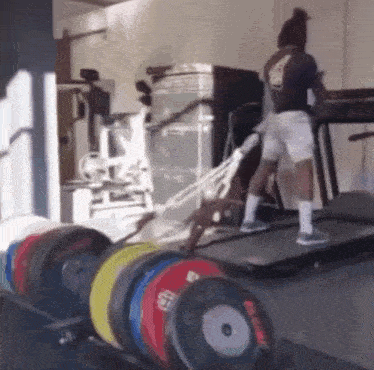 a man is walking on a treadmill in a gym surrounded by weights .