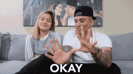 a man and a woman are sitting on a couch with the word okay on the bottom