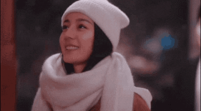 a woman wearing a hat and scarf is smiling and looking up .