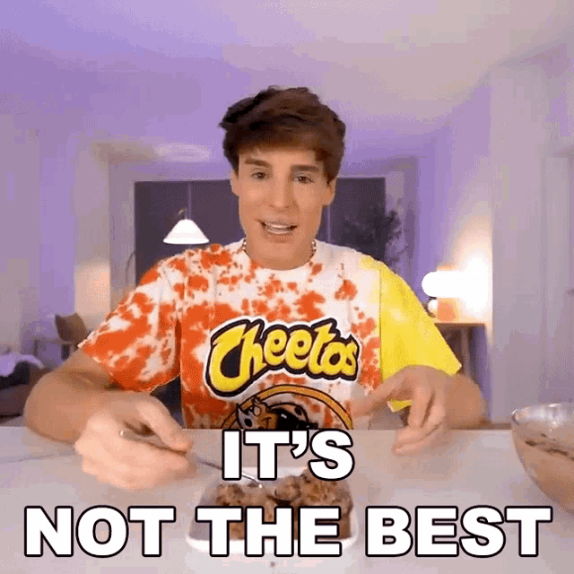 a man wearing a cheetos t-shirt is sitting at a table