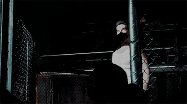 a man in a white tank top is standing in a dark room