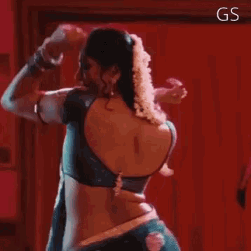a woman in a blue blouse is dancing in front of a red wall with gs written on the bottom