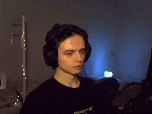 a young man wearing headphones and a black shirt is standing in front of a microphone in a dark room .