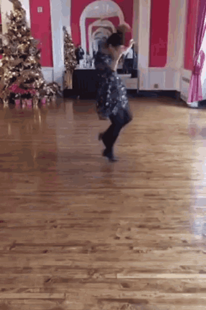 a woman in a black dress is dancing on a wooden floor in front of a christmas tree