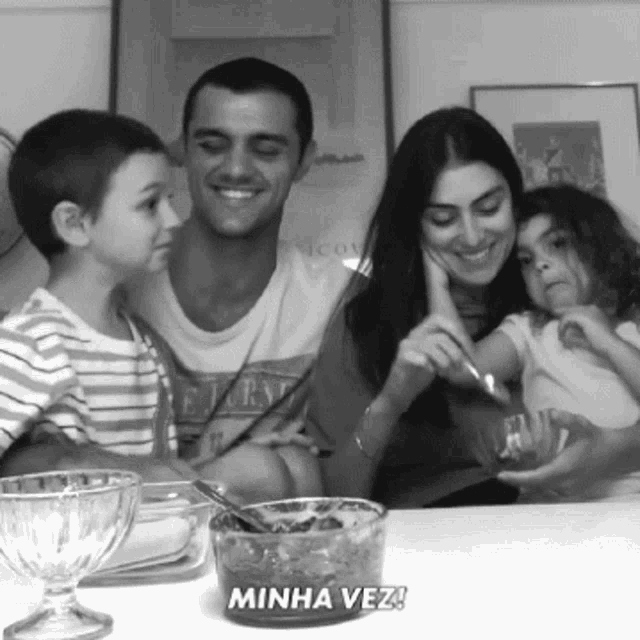 a black and white photo of a family sitting at a table with minha vez written on the bottom
