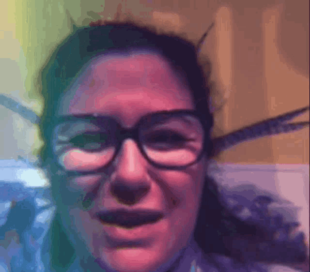 a woman wearing glasses looks at the camera with a purple background