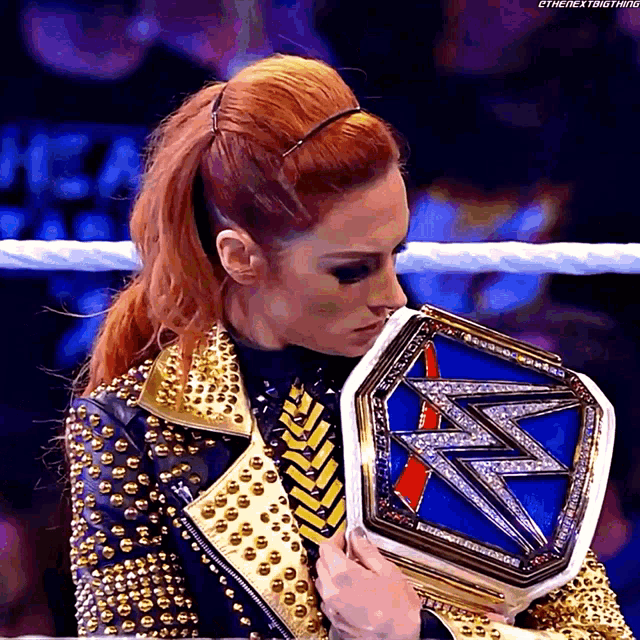 a woman in a studded jacket is holding a wrestling belt