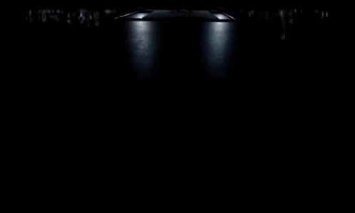 a man in a suit sits in a dark room in front of a table