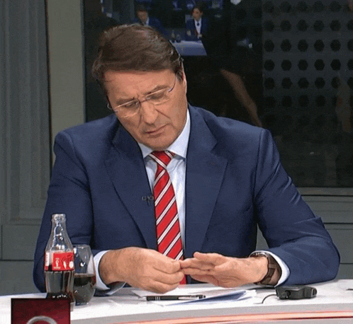 a man in a suit and tie sits at a desk with a coca cola bottle