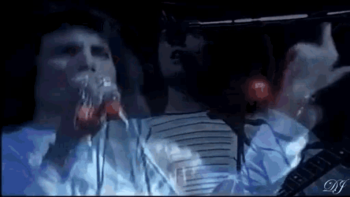 a man is singing into a microphone in a dark room while another man plays a guitar .