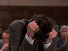 a man in a suit is scratching his head in a crowded room