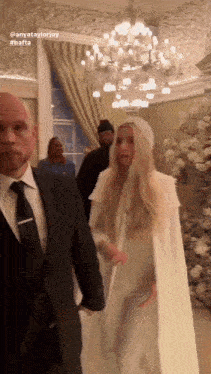 a woman in a white cape is being escorted by a man in a suit and tie