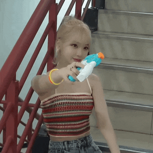 a woman in a striped crop top is holding a blue water gun