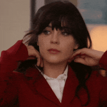 a woman wearing a red jacket and a white shirt adjusts her hair
