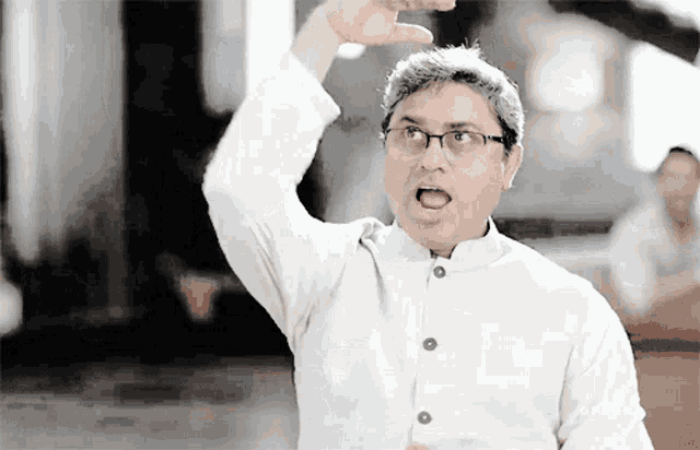 a man wearing glasses and a white shirt is making a gesture with his hand