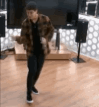 a man in a plaid jacket is dancing in a room with a television .