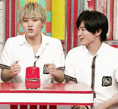 two young men are sitting at a table and talking
