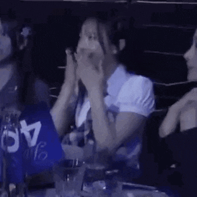 a woman is covering her mouth with her hands while sitting at a table .