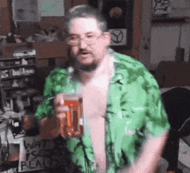 a shirtless man in a green shirt is holding a glass of beer in a room .