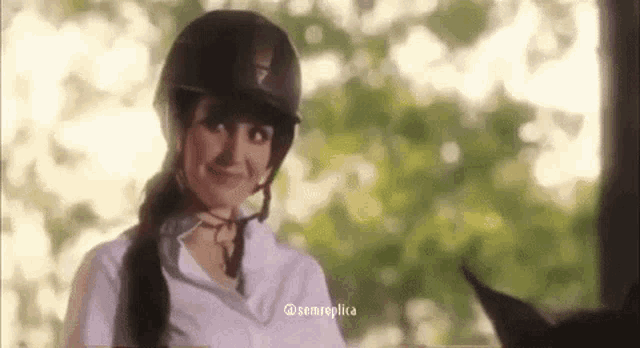 a woman wearing a helmet and a white shirt is riding a horse .
