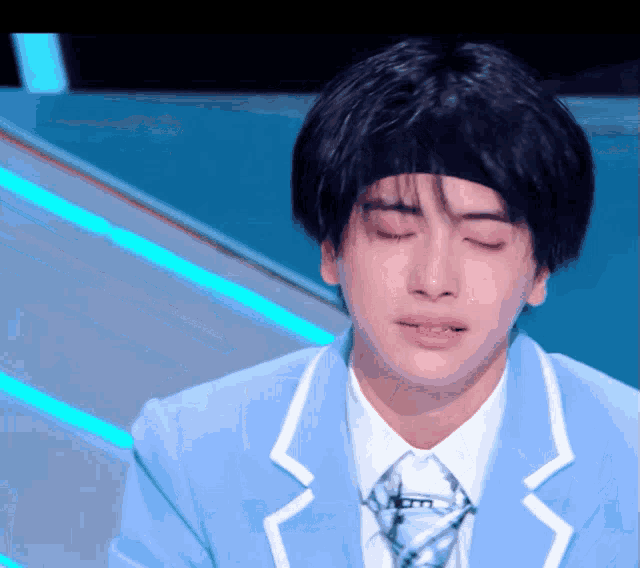 a man in a blue suit and tie is crying with his eyes closed