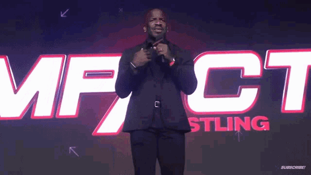 a man in a suit stands in front of a sign that says impact wrestling