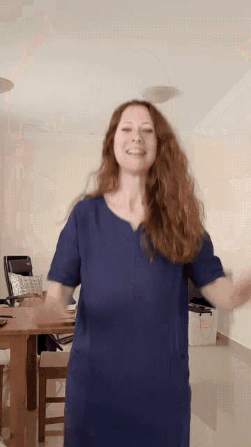 a woman wearing a blue scrub top is dancing in a living room