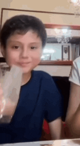 a young boy is sitting at a table with a glass of water in his mouth .