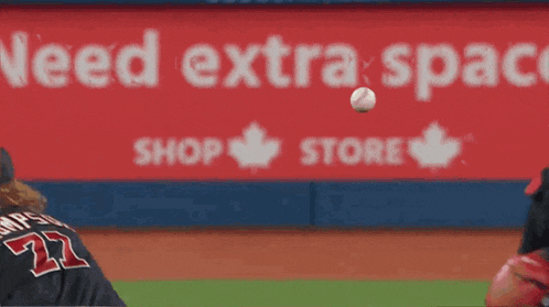 a baseball player catches a ball in front of an advertisement for the blue jays