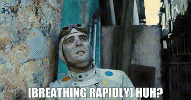 a man wearing a helmet and goggles is leaning against a wall with the words breathing rapidly huh .