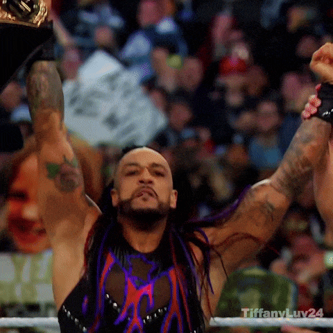 a wrestler with purple hair is holding a championship belt in the air .
